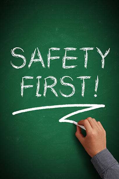 Hand with white chalk writing 'Safety First!' on chalkboard.